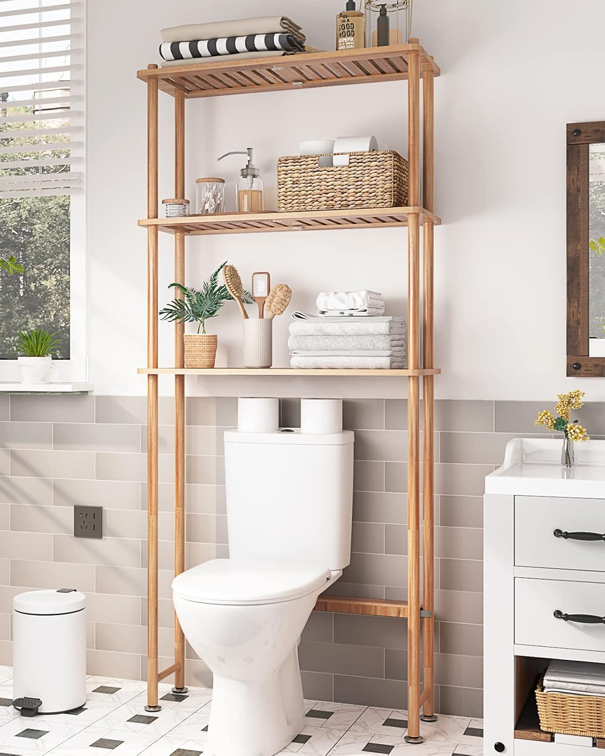 Three-tier bamboo shelf standing over a toilet styled with rolled towels and a plant
